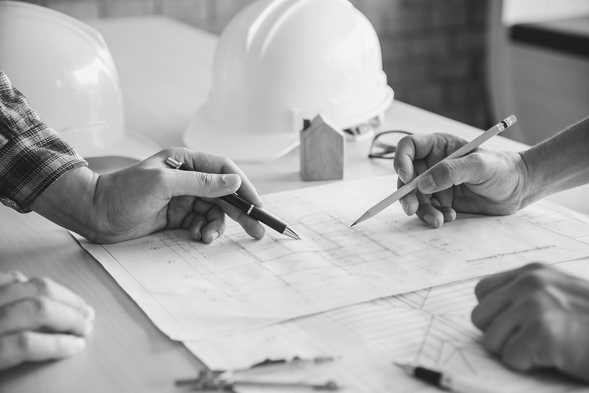 Plan de construction annoté sur une table, avec casques de chantier et maquette